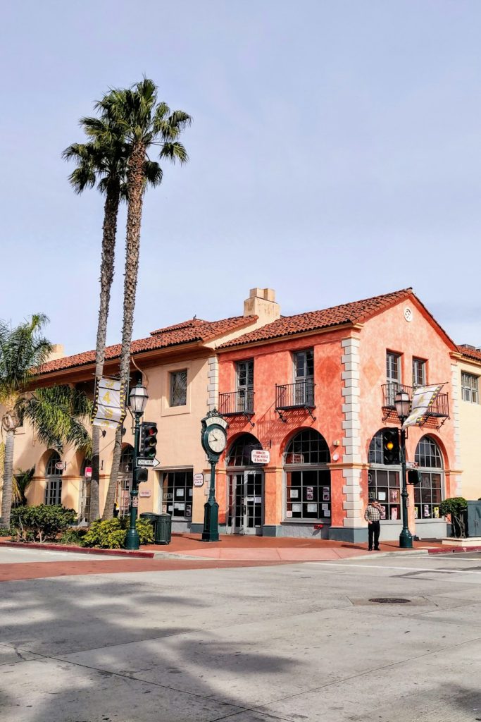 Low-rise stucco commercial building with arches and palms on a street corner
