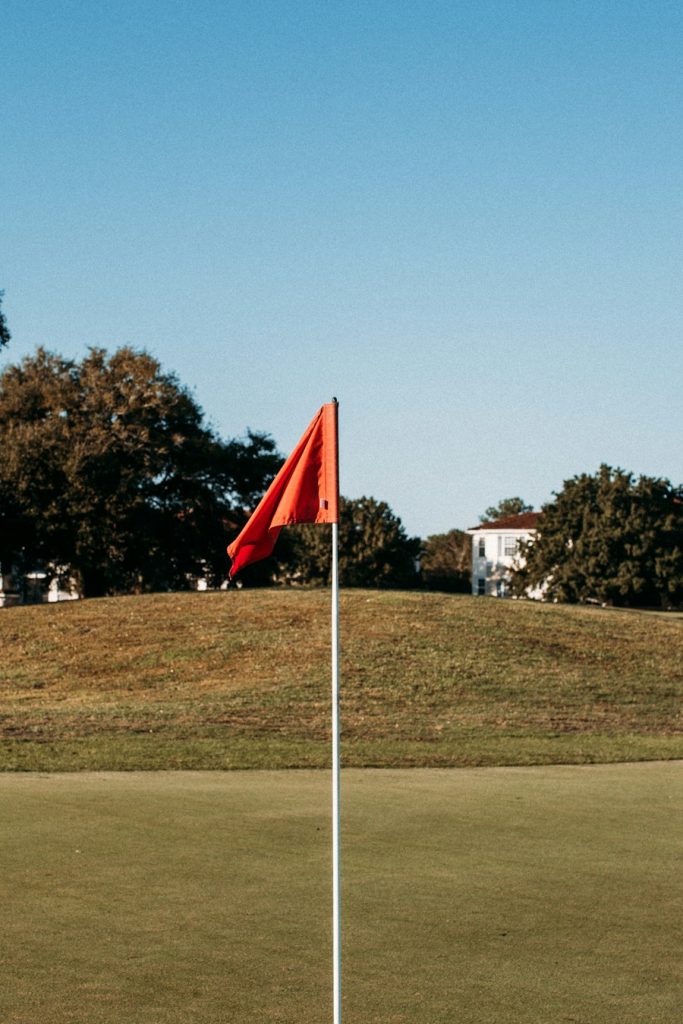 Red flag on a golf green framed by oak trees