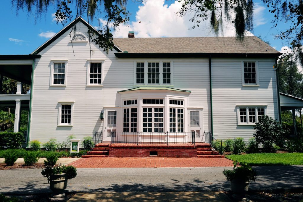 White two-story frame house with a brick front stoop under moss-draped oaks