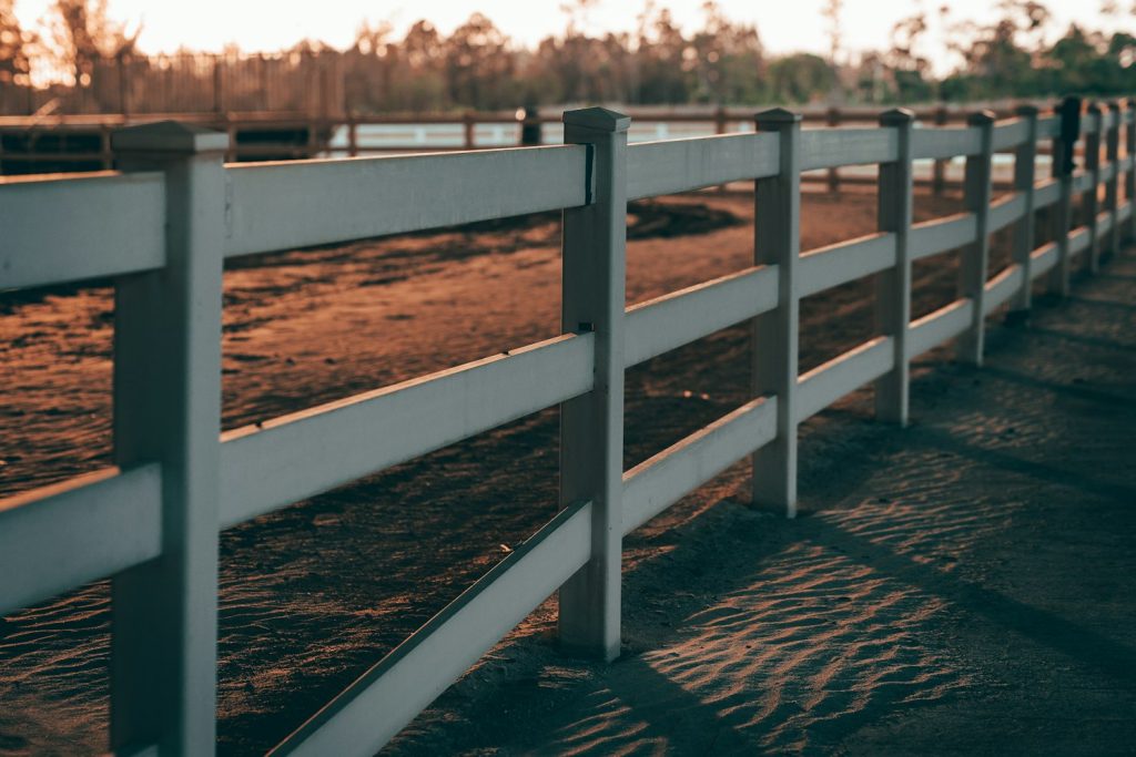 White board fence along a sandy paddock at sunset