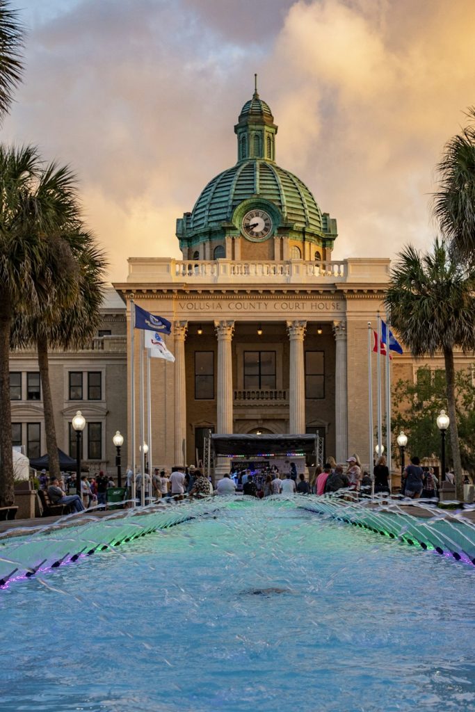 Historic domed county courthouse with palms and a fountain at dusk