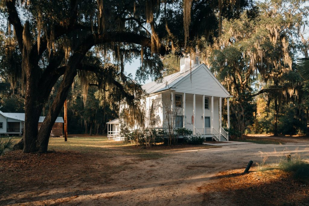 Modest white cottage with a porch under moss-draped oaks
